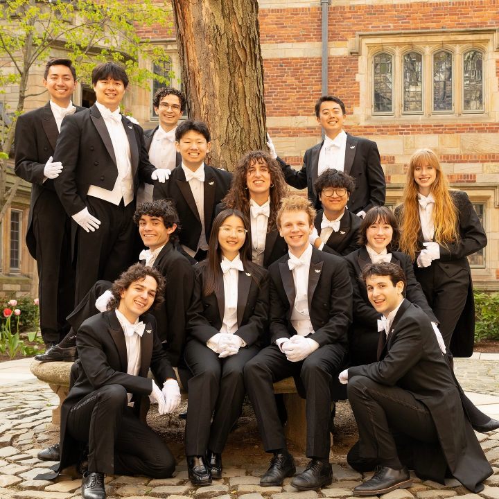 The Whiffenpoofs of 2026 in white tie, gathered around a tree in a Yale courtyard.